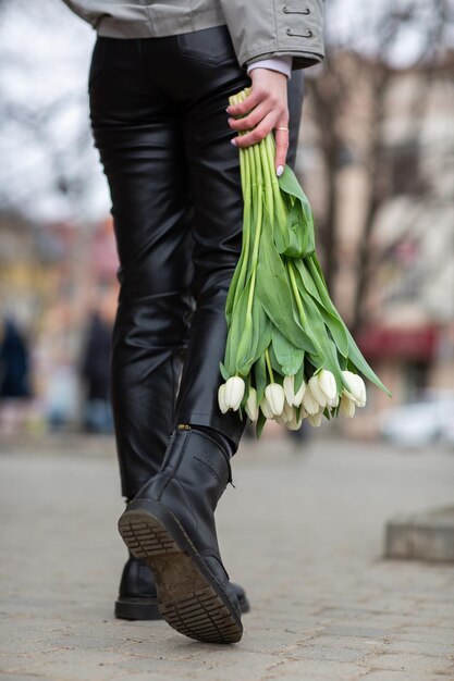 Bouquet of white tulips in the hand of a girl girl holding flowers on the background of beautiful legs spring concept fresh spring colors