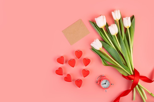 Bouquet of white tulips hearts envelope and a clock on an pastel pink background Time for love