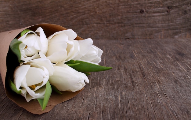 Bouquet of white tulips in kraft paper on an old wooden background