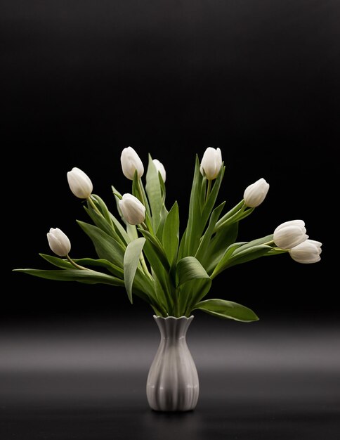 Bouquet of white tulips in a vase on a dark background with perspective