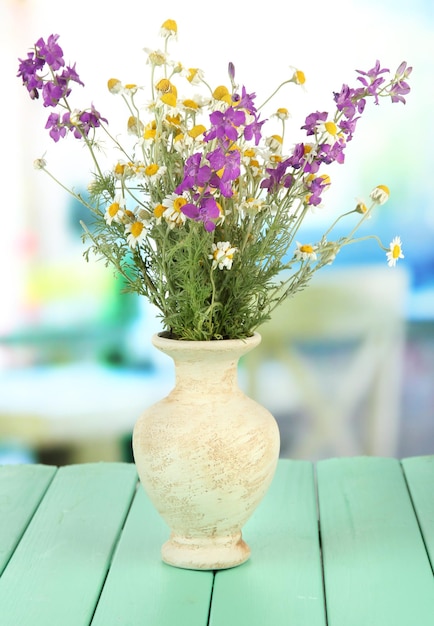 Bouquet of wild flowers in vase on bright background