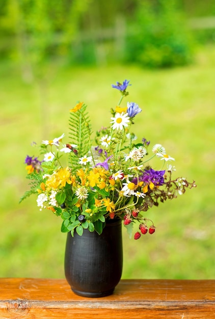 Bouquet of wildflowers and strawberry berries stand on the terrace