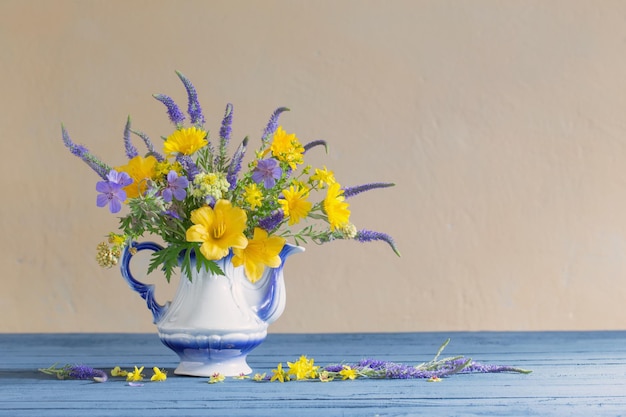 Bouquet with blue and yellow flowers in teapot on wooden table