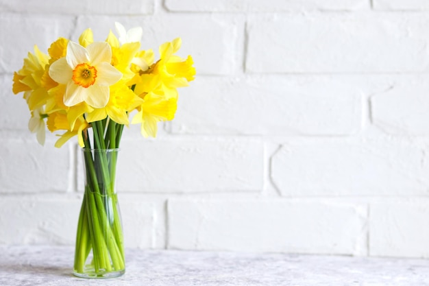 Bouquet of yellow daffodils in a vase against a brick wall Flower arrangement Greeting card