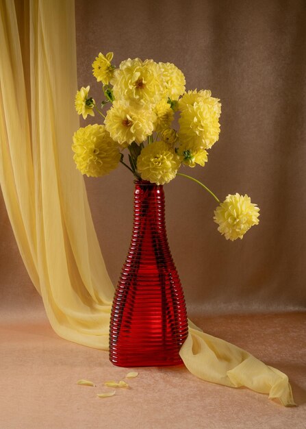 Bouquet of yellow dahlias in a red vase Orange background Yellow scarf Autumn still life