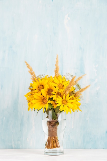 A bouquet of yellow flowers, sunflowers, in a glass vase on blue. Copy space.