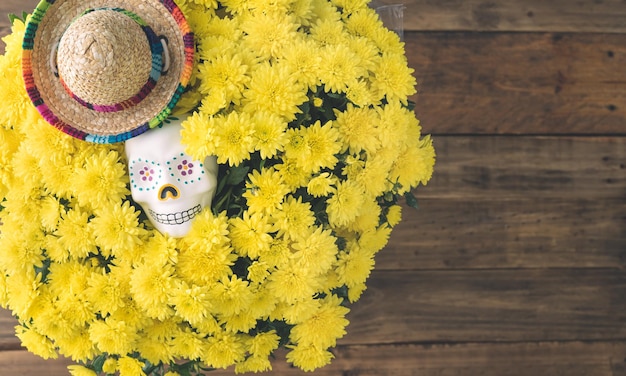 Bouquet of yellow flowers with skull and Mexican hat on wooden background Space Day of the dead in Mexico