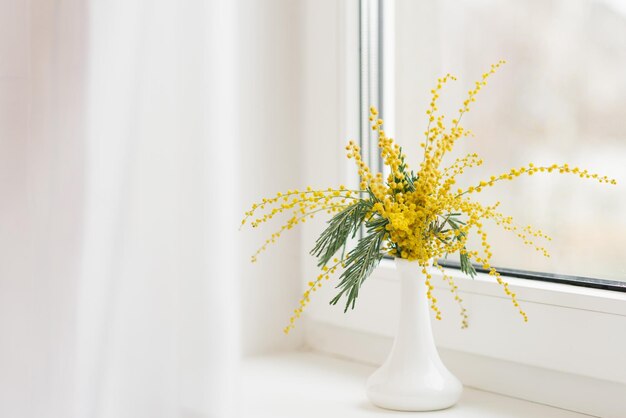 Bouquet of yellow mimosa flowers on a white windowsill during the day