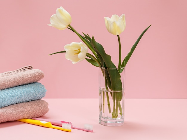 Bouquet of yellow tulips in a glass vase, stacked towels and toothbrushes on pink