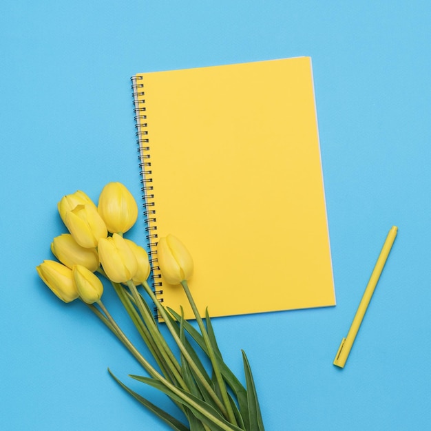 A bouquet of yellow tulips a yellow notebook and a yellow pen on a blue background Minimal concept