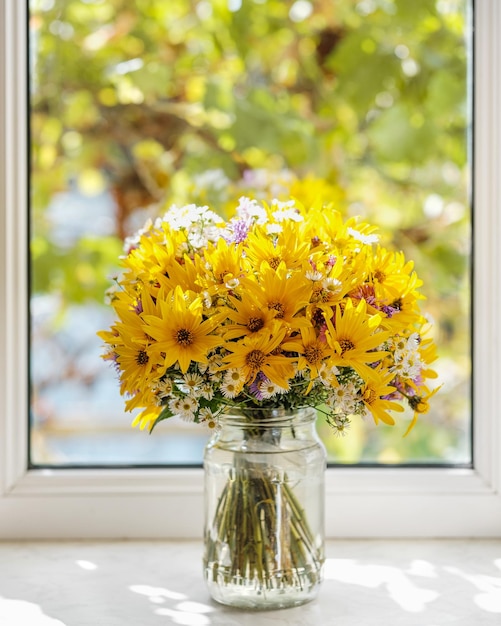 Bouquet of yellow violet and white wild flowers in a jar against window Autumn composition