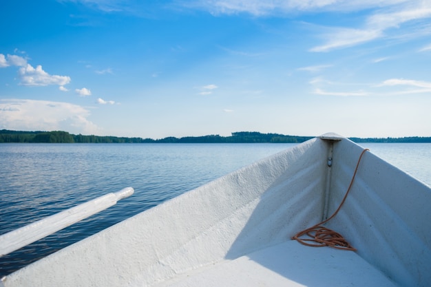 The bow of a white rowing boat on a smooth blue lake, looking at the horizon somewhere in the depths of Finland, a good summer day. Vacation on the lake.