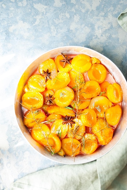 A bowl of apricots with rosemary and thyme on a blue background.