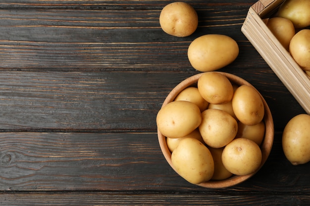 Bowl and basket with young potatoes on wooden surface