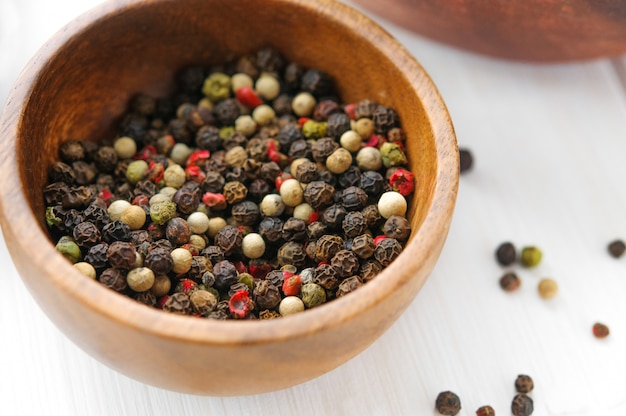 Bowl of black, white and red pepper on white wooden table