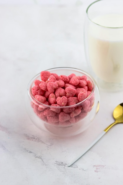 A bowl of breakfast cereal and a glass of milk on a white marble background Snacks with raspberry flavor