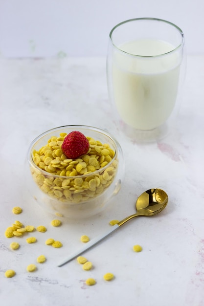 A bowl of breakfast cereal and a glass of milk on a white marble table Instant corn flakes with strawberries