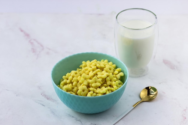 A bowl of breakfast cereal and a glass of milk on a white marble table Instant corn flakes