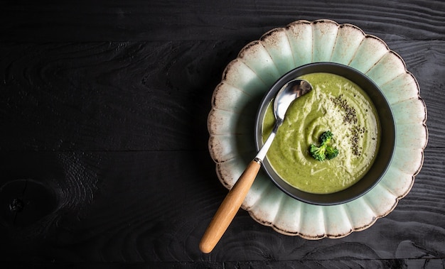 Bowl of broccoli cream soup with parmesan cheese and crunchy croutons on wooden table top view