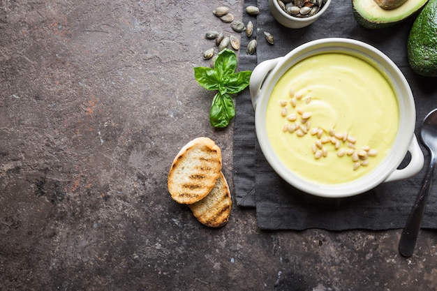 Bowl of broccoli and green peas cream soup in a white bowl with avocado, top view