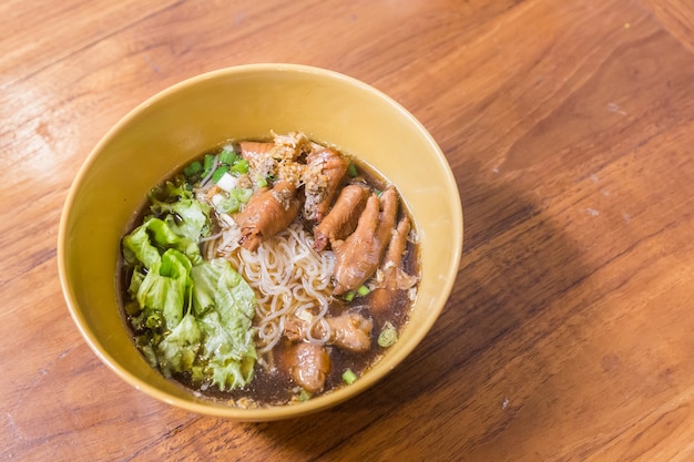 Bowl of chicken noodle soup with vegetables on wood table