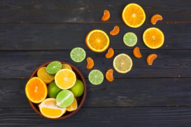 Bowl of citrus fruits on black wooden table, top view