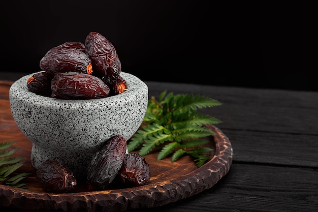 Bowl of dried dates on dark wooden background from side view