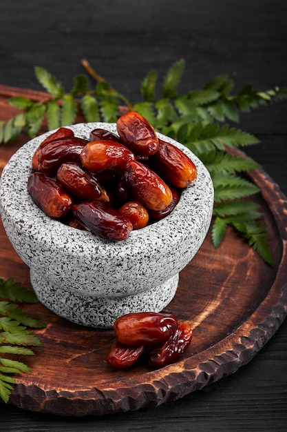 Bowl of dried dates on dark wooden surface from side view