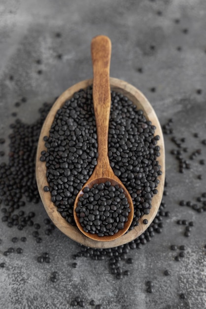 Bowl of dry black lentils beans with a spoon on grey table close up protein source for vegetarian diet