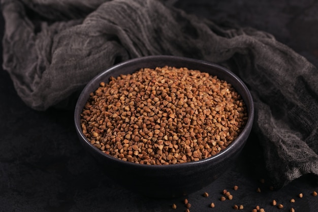 Bowl of dry raw buckwheat groats on a dark. Cooking buckwheat porridge concept.