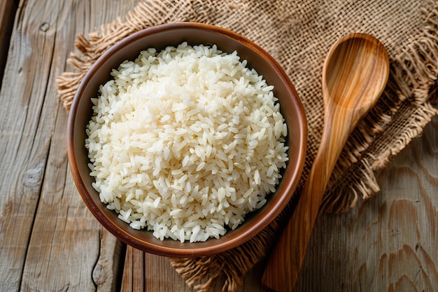 A bowl filled with cooked white rice sits on a wooden table next to a wooden spoon Generative AI