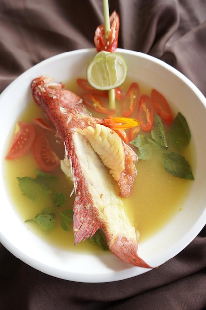 A bowl of fish soup with a lemon slice on top