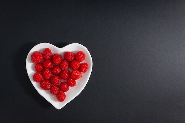 Bowl of fresh raspberries in a heart-shaped bowl isolated on the black surface