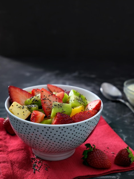 A bowl of fruit salad with a spoon on a red napkin.