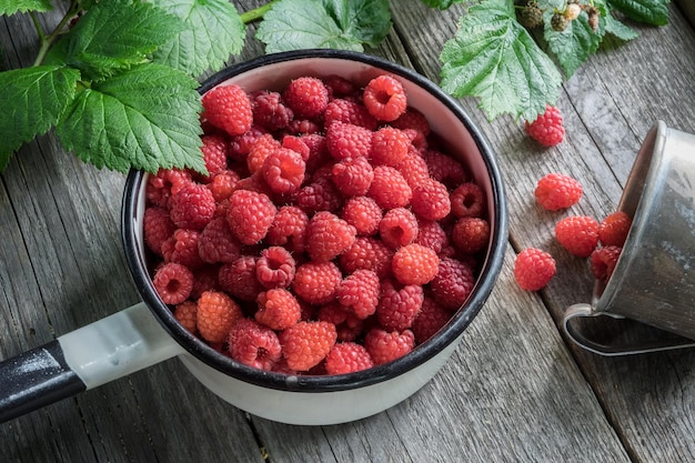 Bowl full of raspberries and rustic mug with ripe scattered berries Top view