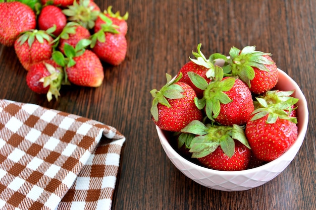 A bowl of garden strawberries next to a checkered towel on kitchen table