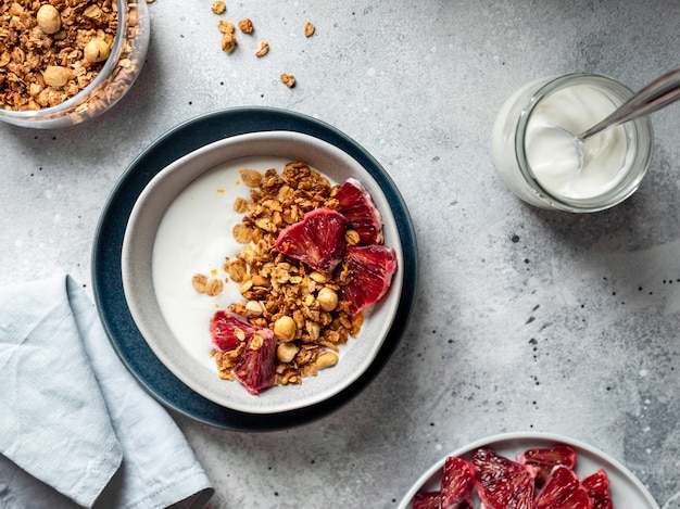 Photo bowl of greek yogurt, granola and bloody orange on a gray surface. healthy breakfast concept. horizontal image, copy space, table top view.