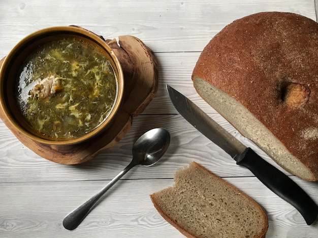 Photo a bowl of green sorrel borscht soup and a spoon a knife and bread for breakfast or lunch