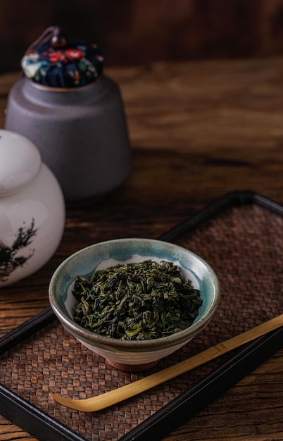 A bowl of green tea sits on a tray next to a teapot and a teapot.