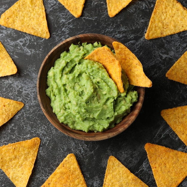 Bowl of guacamole and chips on black smokey background, top view