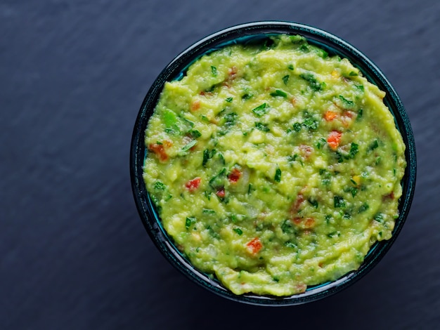 Bowl of guacamole on a dark background. Traditional mexican dip sauce guacamole. Traditional mexican food. Copy space. Top view