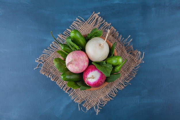 Bowl of healthy white and red radishes with greens on blue surface.