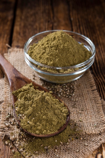 A bowl of henna powder sits on a wooden table next to a spoon with the word henna.