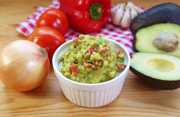 Bowl of Homemade Guacamole with Fresh Avocadoes Onions and Tomatoes Around