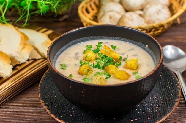 A bowl of homemade mushroom puree soup with herbs and bread on a wooden table Homemade vegetarian mushroom soup with vegetables and bread