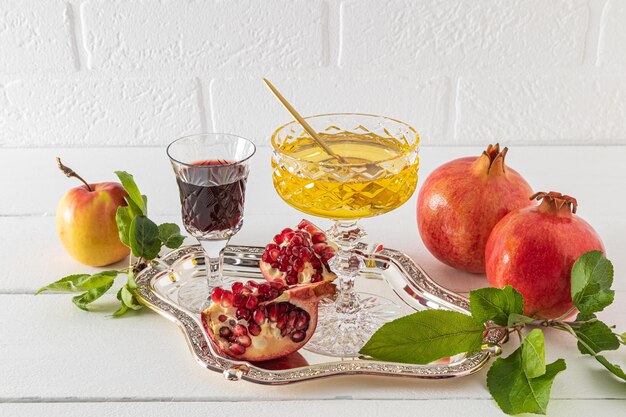 A bowl of honey a glass of red wine ripe pomegranates and apples on a silver tray against a white brick wall The concept of the of Rosh Hashanah