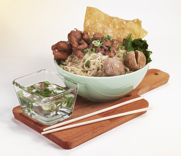 A bowl of Indonesian chicken noodles with chicken, claws, meatballs, mustard greens and scallions