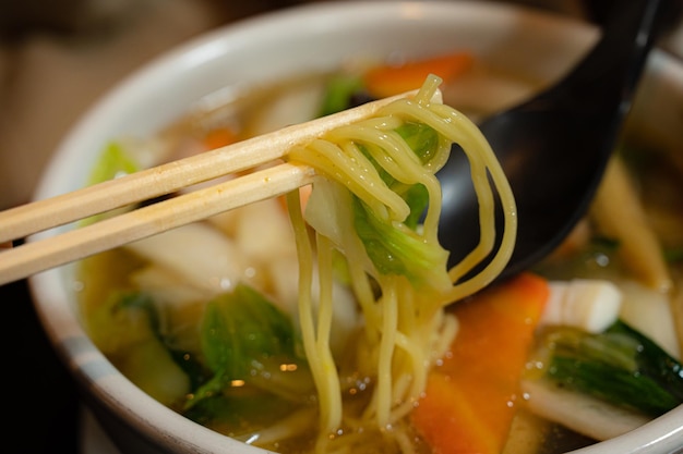 A bowl of noodles with a pair of chopsticks holding a fork.