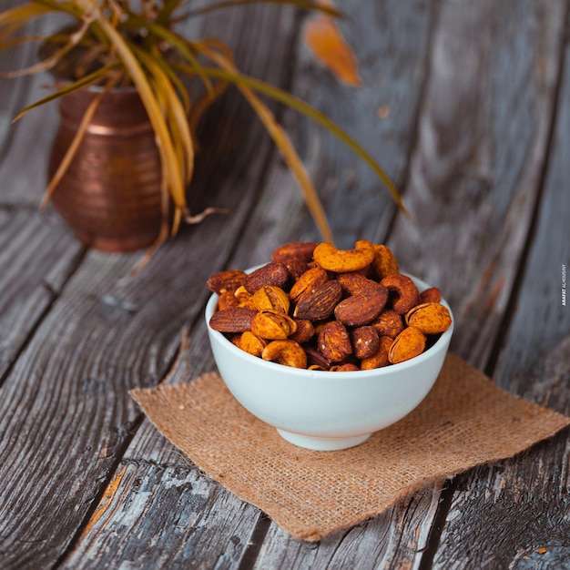 A bowl of nuts is on a table next to a potted plant.