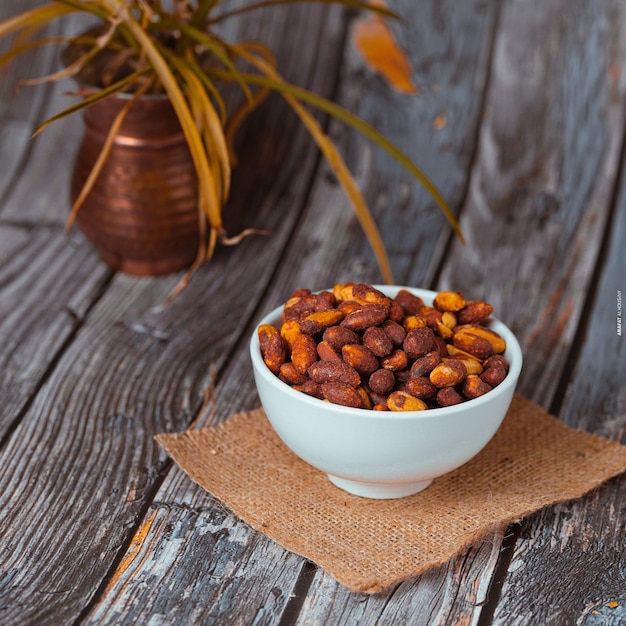 A bowl of nuts is next to a vase with a plant in it.